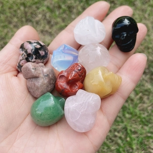 Natural hand-carved crystal skull figurines in various gemstones held in hand over grass