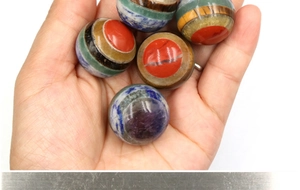 Close-up of five 20mm colorful layered gemstone spheres held in hand with a polished finish