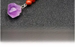 Detailed macro of natural raw amethyst crystal pendant on a red beaded keyring strap