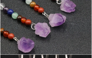 Close-up of natural amethyst raw stone pendant with colorful chakra beads on black background
