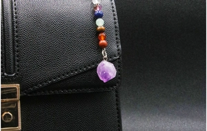 Detail of a natural amethyst crystal pendant with colorful beads on a black leather bag