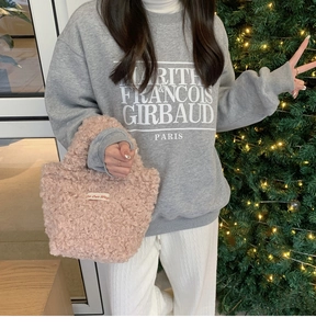 Pink plush mini tote bag with a small woven label shown in a cozy holiday home setting