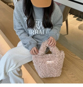 Detailed close-up of pink curly plush mini handbag with text label held by a model