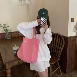 Pink canvas tote bag with letter print detail shown in a cozy cafe setting OOTD