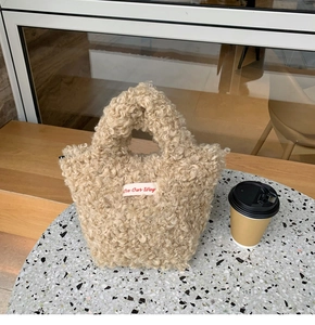 Close-up of khaki plush mini handbag with On Our Way embroidery on a cafe table
