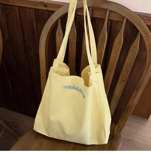 Detail of light yellow canvas tote bag with blue embroidered letters on a wooden chair