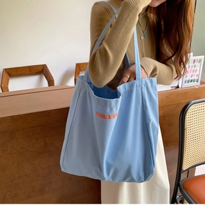 Blue canvas tote bag with orange maaa letters worn over shoulder in cafe setting