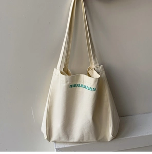 Detailed close-up of dark green maaaaaas embroidery on a cream cotton canvas tote bag