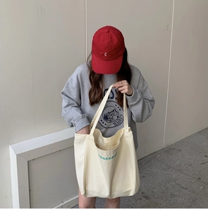 Detail of cream canvas tote bag featuring green letter embroidery and outer pocket