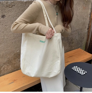 Detail of cream canvas tote bag featuring green maad embroidery and sturdy shoulder straps