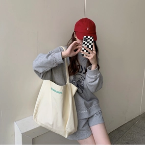 Detail of cream canvas tote bag with green embroidered maaaaaaas letters on model