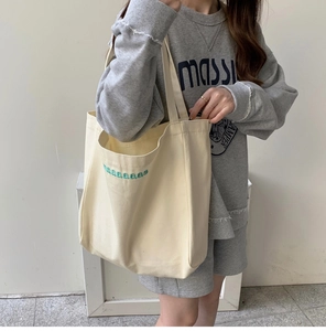 Close-up of cream canvas tote bag featuring green naaaaaas letter embroidery detail