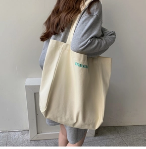 Detail of a large cream canvas tote bag featuring green maaa embroidered lettering