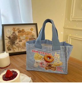 Dettaglio borsa pranzo a quadretti blu con orsetto e ciambelle su tavolo in legno