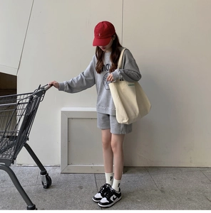 Close-up of beige canvas tote bag paired with grey knit sweatshirt and red baseball cap