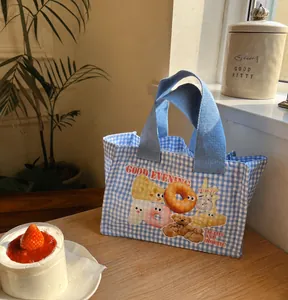 Dettaglio della borsa termica a quadretti blu con orsetto e ciambelle su tavolo