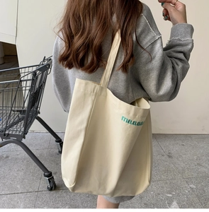 Outdoor shot of a cream canvas tote bag with green embroidered letters on the shoulder
