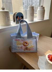 Dettaglio della borsa pranzo a quadretti blu con orsetto su un tavolo di legno