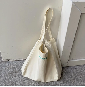 Detailed close-up of cream canvas tote bag featuring green embroidered arched letters