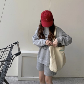 Close-up of ivory canvas tote bag paired with grey tracksuit and red baseball cap