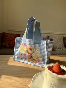 Dettaglio della borsa da pranzo a quadretti blu con illustrazioni di orsetto e ciambella al sole