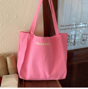 Detail shot of a bright pink canvas tote bag with yellow maaas lettering in a cafe