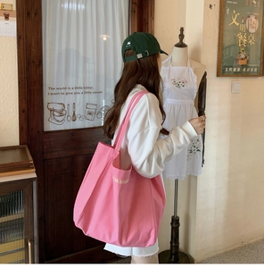 Pink canvas tote bag with embroidered letters shown in a cozy indoor lifestyle setting