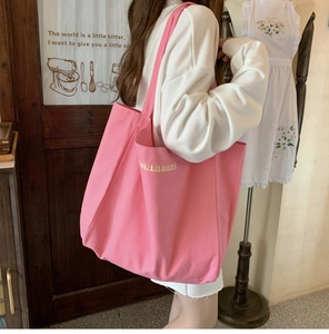 Pink canvas tote bag with embroidered letters shown on model in a cozy indoor setting
