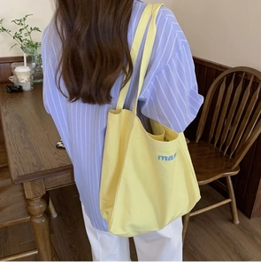 Detail of vibrant yellow canvas tote bag with blue 'ma' text shown in a lifestyle setting