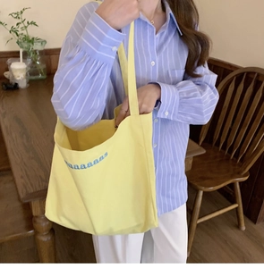Close-up of bright yellow canvas tote bag with blue letter embroidery for student use