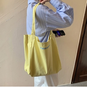 Detail of yellow canvas tote bag with blue embroidered letters and durable texture