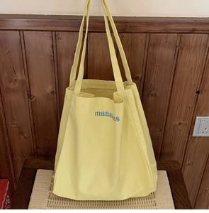 Close-up of bright yellow canvas tote bag with blue maaaaaas embroidery on a chair