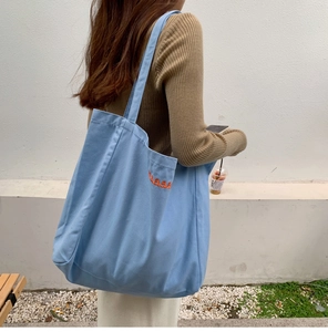 Detailed orange embroidered lettering on a light blue canvas tote bag fabric