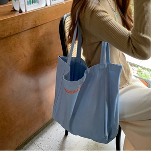 Sky blue canvas tote bag with orange embroidery shown in a warm lifestyle setting