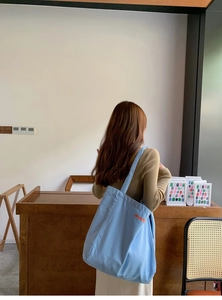 Back view of a light blue canvas tote bag with orange lettering for daily use