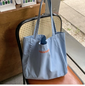 Detail of blue canvas tote bag with orange maaaaa embroidery on a wooden chair