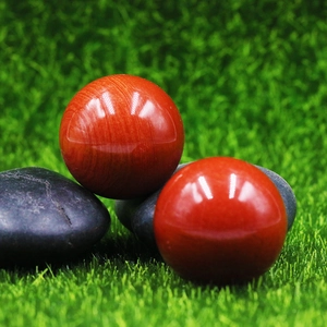 Polished 25mm natural red jasper stone spheres on dark pebbles with grass background