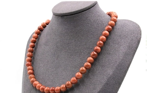 Close-up of sparkling golden sand stone round beads on a grey velvet display stand