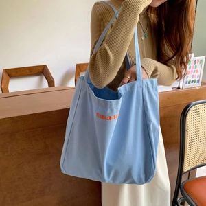 Light blue canvas tote bag with orange maaaa embroidery shown in a cozy wooden cafe
