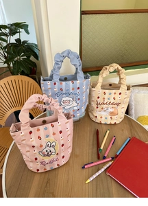 Detail of canvas bucket bags with cartoon prints and ruffled pleated handles on wood table