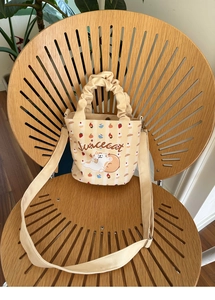 Detail of fluffy cat print and pleated handle on cream canvas bucket bag with strap