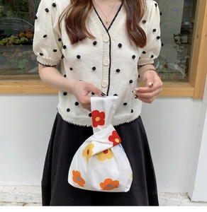 Close-up of Japanese floral wrist bag styled with a polka dot knit sweater and black skirt