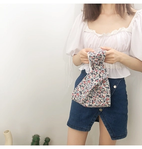 Close-up of a Japanese style floral wrist bag held by a model in a casual outfit