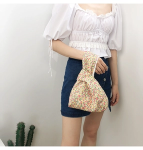 Floral print fabric wrist bag with Japanese knot design shown in a hand-held lifestyle shot