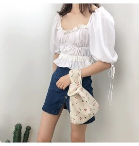 Close-up of beige canvas knot bag with red cherry prints paired with denim skirt