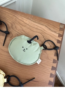 Detail view of a cute apple-shaped green plush earphone pouch with black lanyard on wood