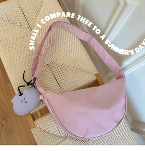 Pink crescent shoulder bag with cute purple cartoon charm on a woven bench
