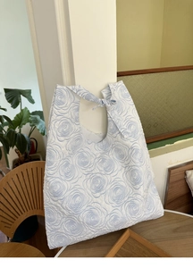 Detail of blue rose embossed quilted tote bag with decorative bow handles and soft texture