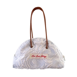 White quilted tote bag with blue floral embroidery and On Our Way red text patch