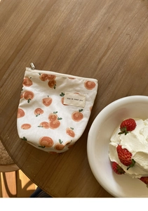 Detail van een mini katoenen tasje met oranje perzikpatronen en een zilveren ritssluiting
